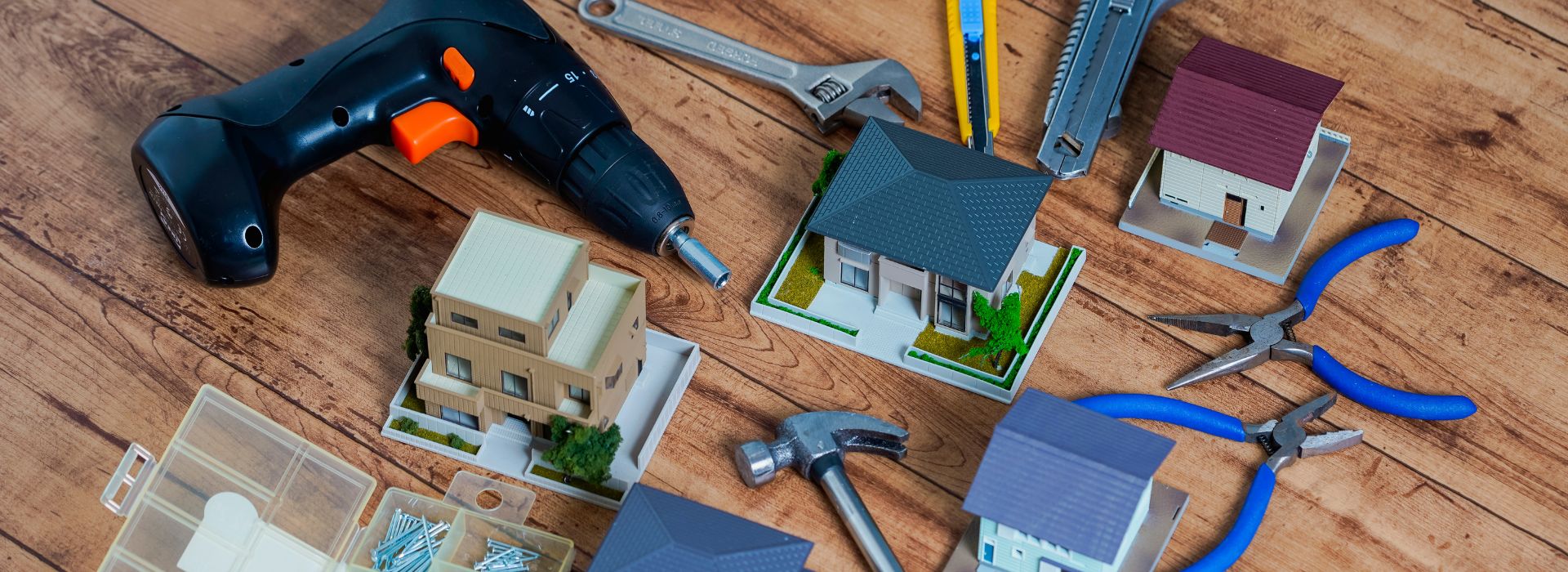 Miniaturas de casas residenciais e ferramentas de construção (furadeira, chave inglesa, martelo, alicates) organizadas sobre uma mesa de madeira rústica, simbolizando reforma e construção civil, iluminação natural quente, foto realista em ângulo alto