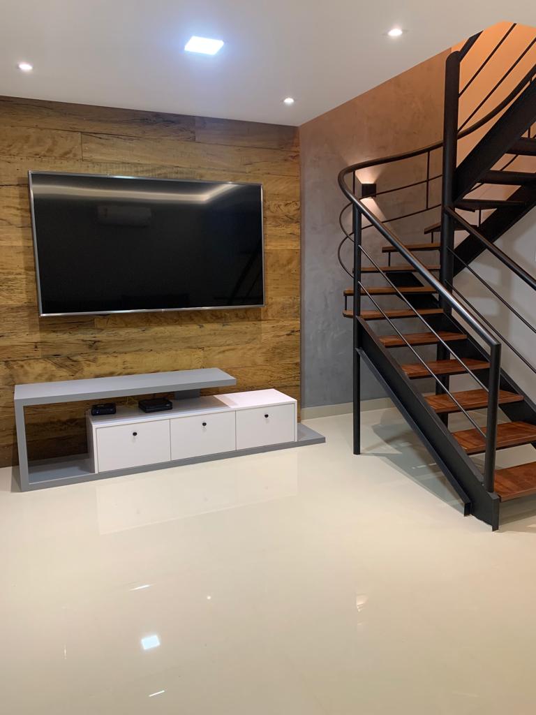 Sala de estar reformada com marcenaria sob medida integrando TV de parede e escada de design com degraus em madeira e estrutura em metal preto, piso porcelanato claro, iluminação embutida no teto, fotografia realista de ambiente de alto padrão